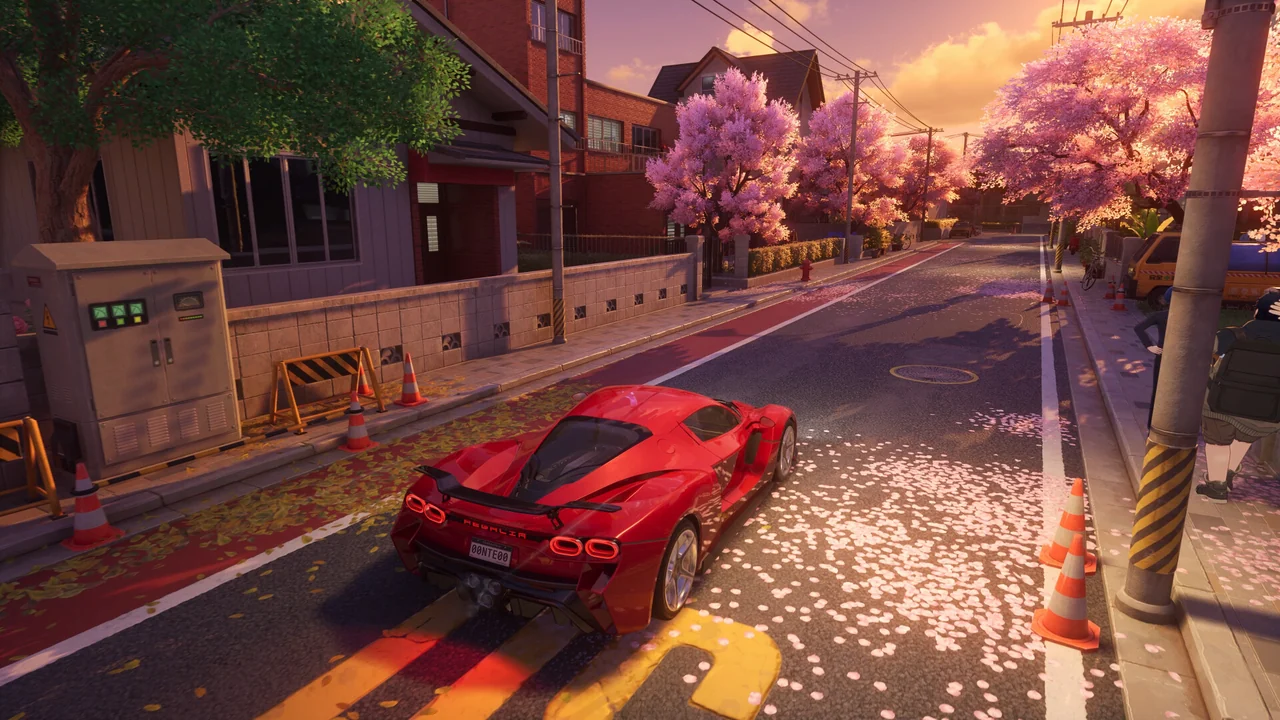 A red sports car on a quiet street strewn with cherry petals beside orange traffic cones at sunset.